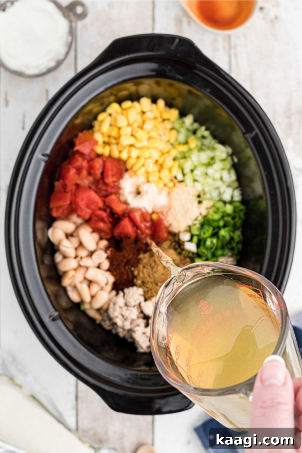 Chicken broth being carefully poured into a crock pot already brimming with chili ingredients.