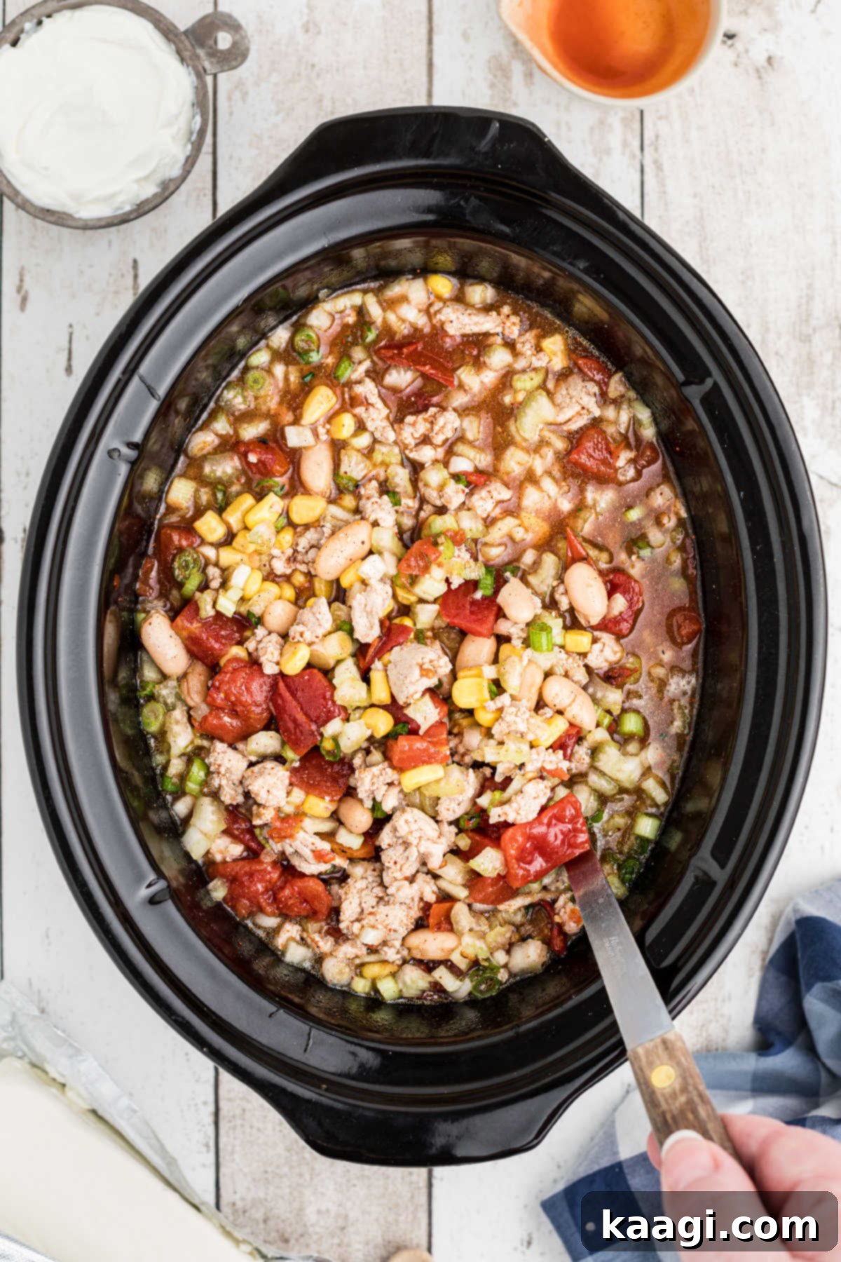 A slow cooker filled with a medley of ingredients being thoroughly stirred to combine flavors.