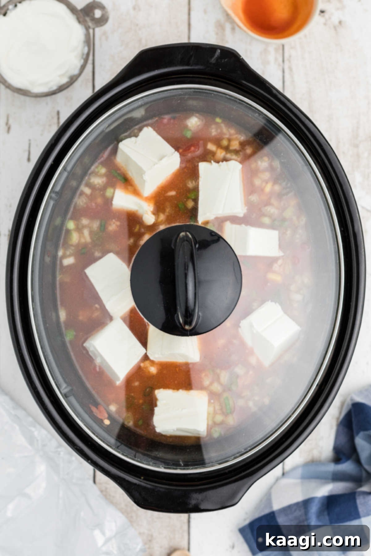 A slow cooker with its lid securely in place, allowing the cream cheese to melt and blend into the buffalo chicken chili.