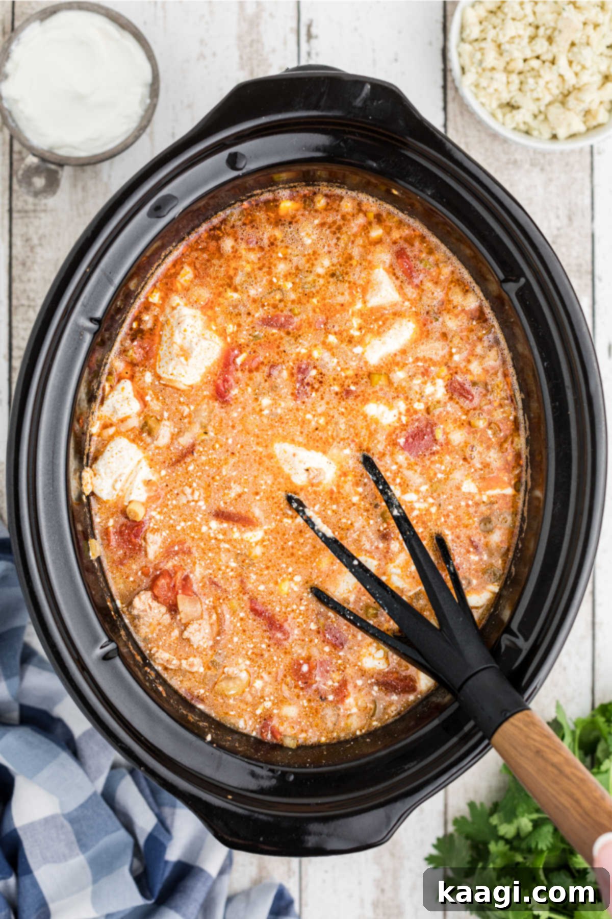 The melted cream cheese being stirred vigorously into the slow cooker buffalo chicken chili until fully integrated and smooth.