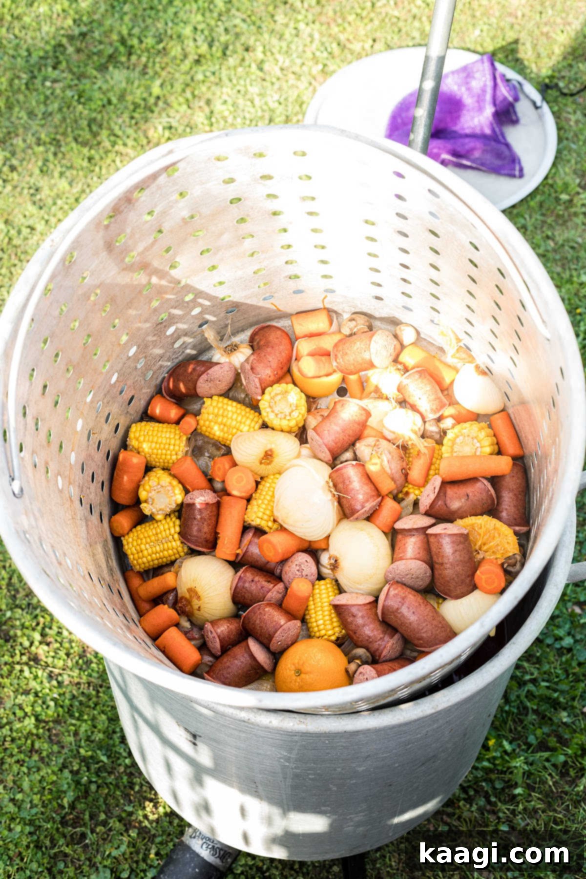 A large boiling pot with basket filled with cooked vegetables and sausage.