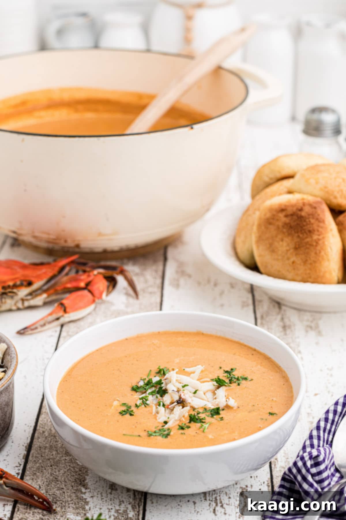 a bowl full of crab soup with a pot in the background and a boiled crab - the bowl of crab soup has crab meat sprinkled on top