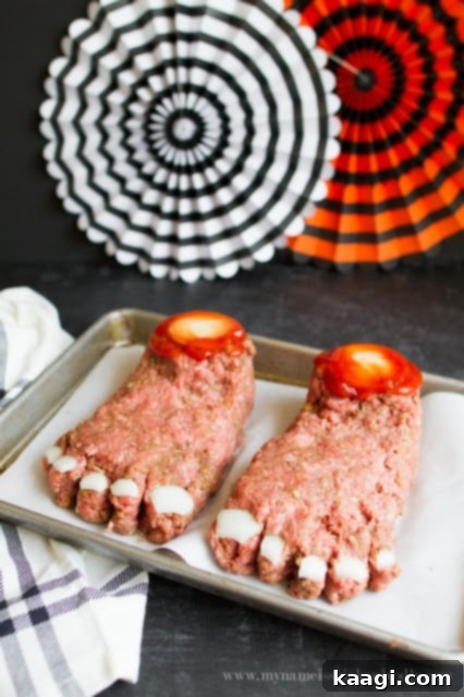 A ghastly Halloween Feet Loaf, creatively shaped from ground meat to resemble a severed foot, adorned with white cheese cut into bone shapes and a 'bloody' tomato sauce for a spooky BBQ treat.