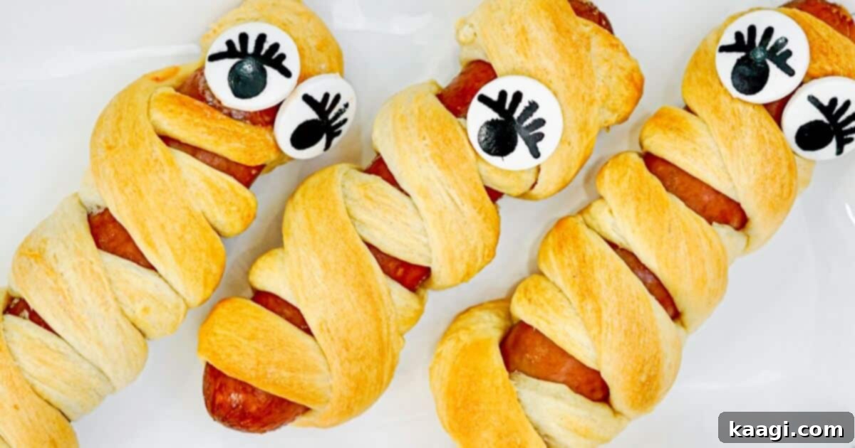 A spooky Halloween Mummy Hot Dog, crafted from a sausage wrapped with crescent dough strips to resemble a mummy, complete with edible googly eyes for a fun, kid-friendly treat.