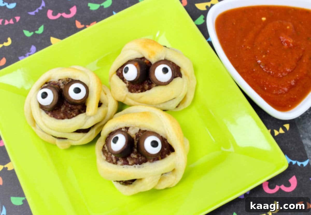 Spooky Mummy Meatballs Halloween Appetizer, featuring meatballs wrapped in pastry strips to look like mummified heads, adorned with edible googly eyes for a fun, quick party bite.
