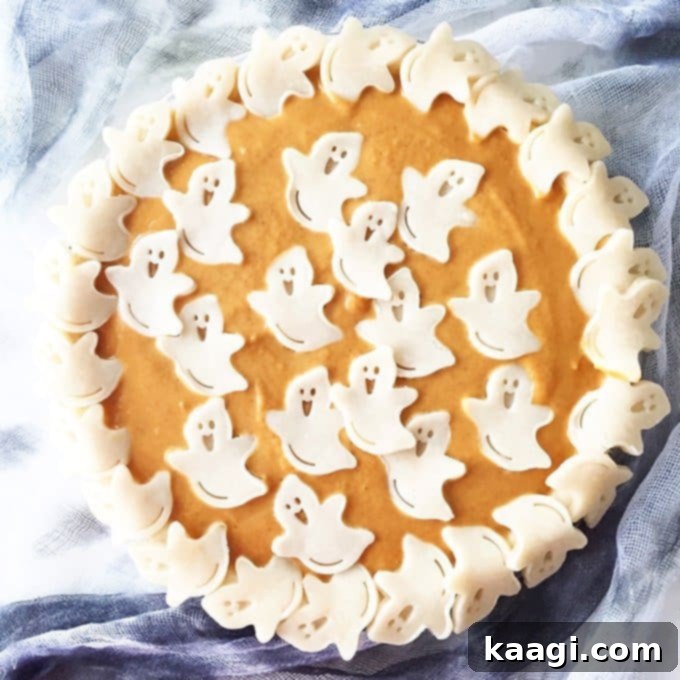 A traditional pumpkin pie whimsically decorated with ghost shapes cut out of pastry on top.