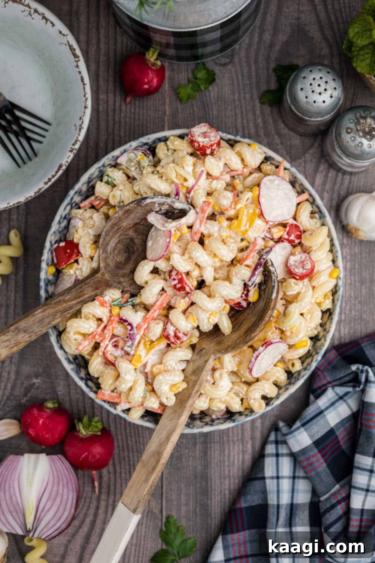 A vibrant late summer pasta salad with serving utensils ready to scoop, showcasing fresh vegetables and creamy dressing.