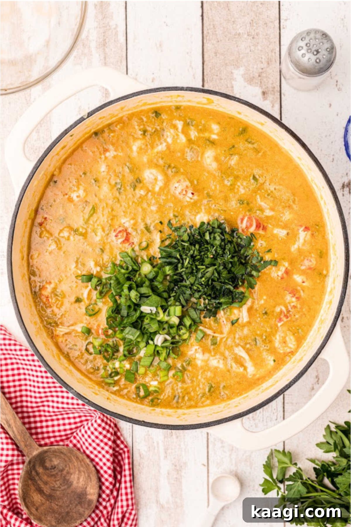 Green onions and chopped parsley have been added to a large Dutch oven with crawfish etouffee cooking.