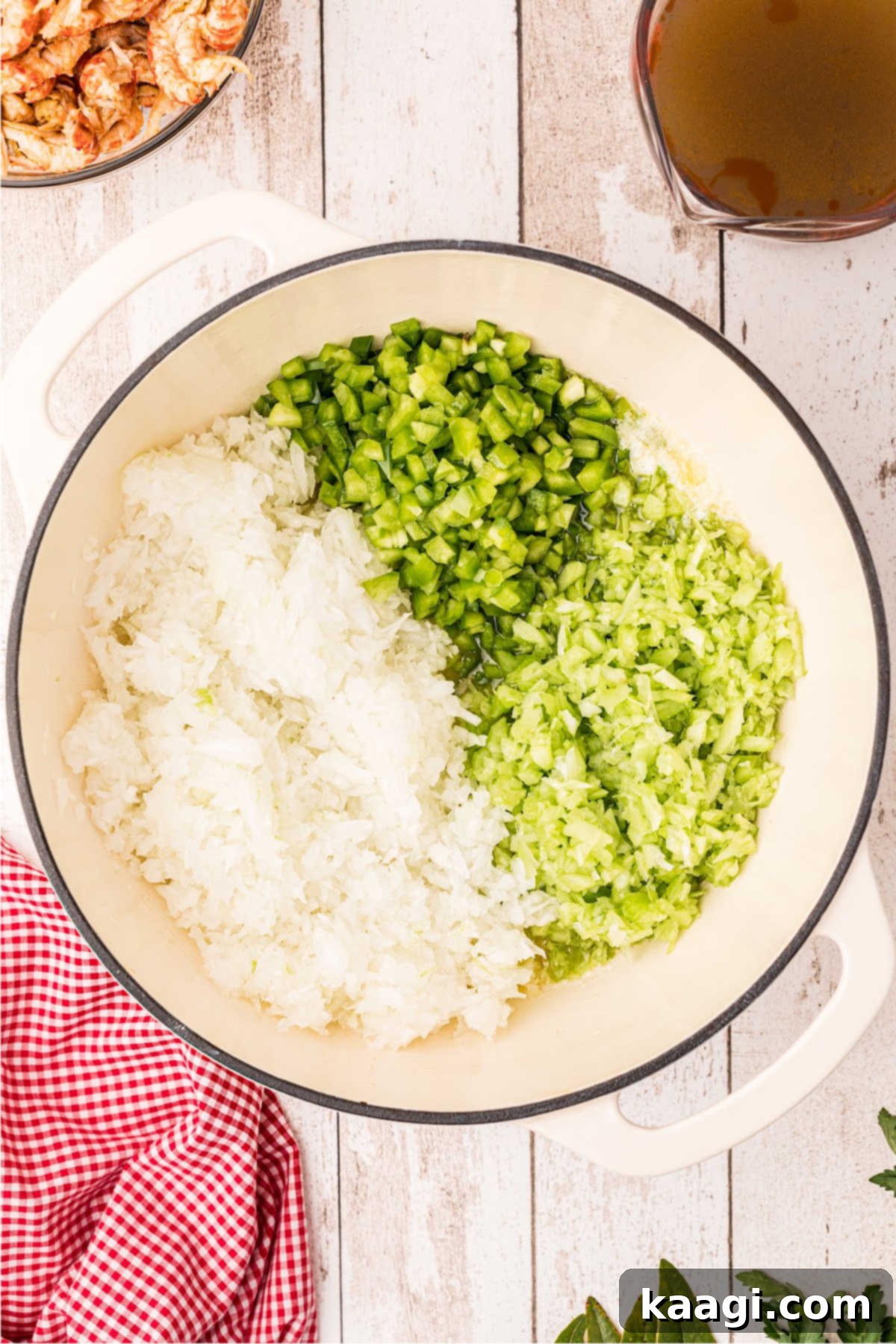 An overhead view of a large Dutch oven with onions, bell peppers and celery.