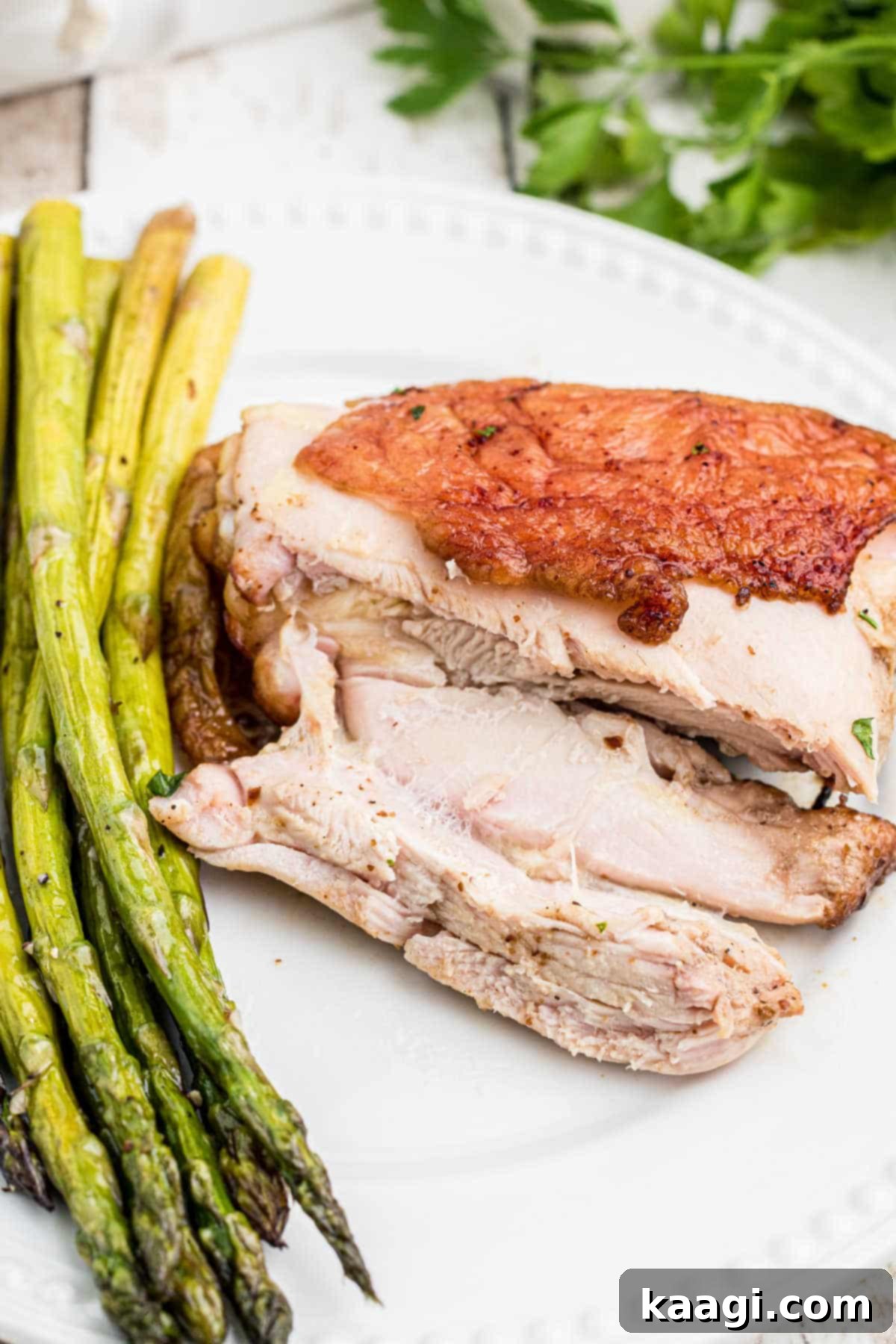 A beautifully presented dish of perfectly smoked chicken thighs, sliced to show the tender meat, served with vibrant green asparagus.