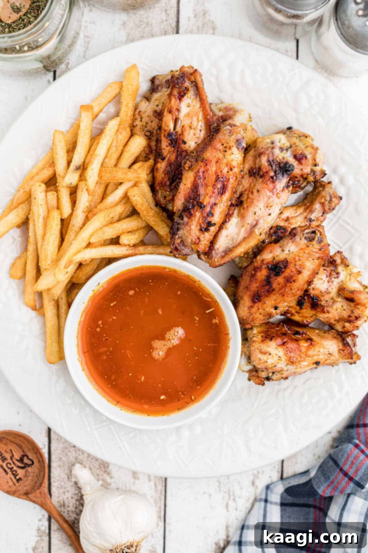 Overhead shot of a plate of golden brown chicken wings, crispy french fries, and a small bowl of rich Cajun butter sauce for dipping.