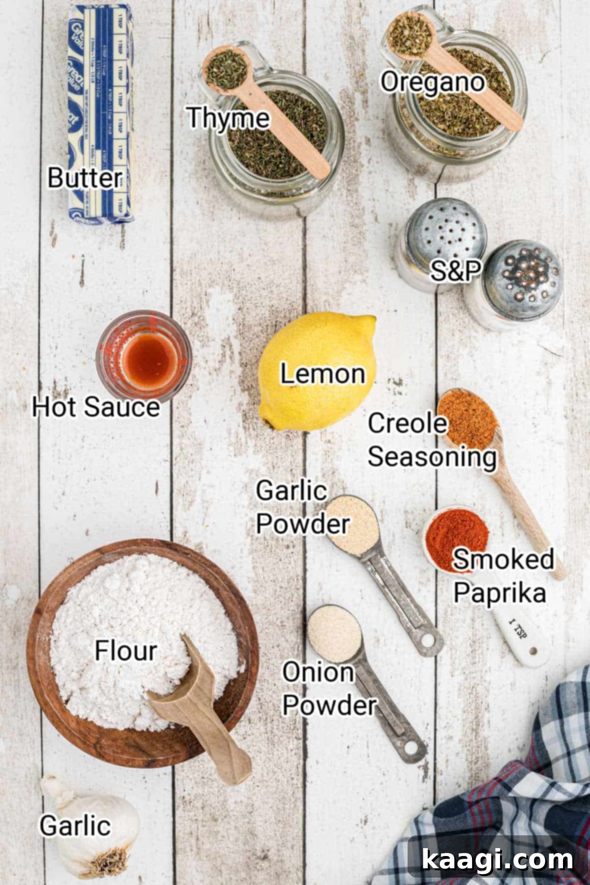 A collection of essential ingredients neatly laid out on a kitchen counter, showcasing unsalted butter sticks, fresh garlic cloves, a whole lemon, and various spice jars needed for the Cajun butter sauce.