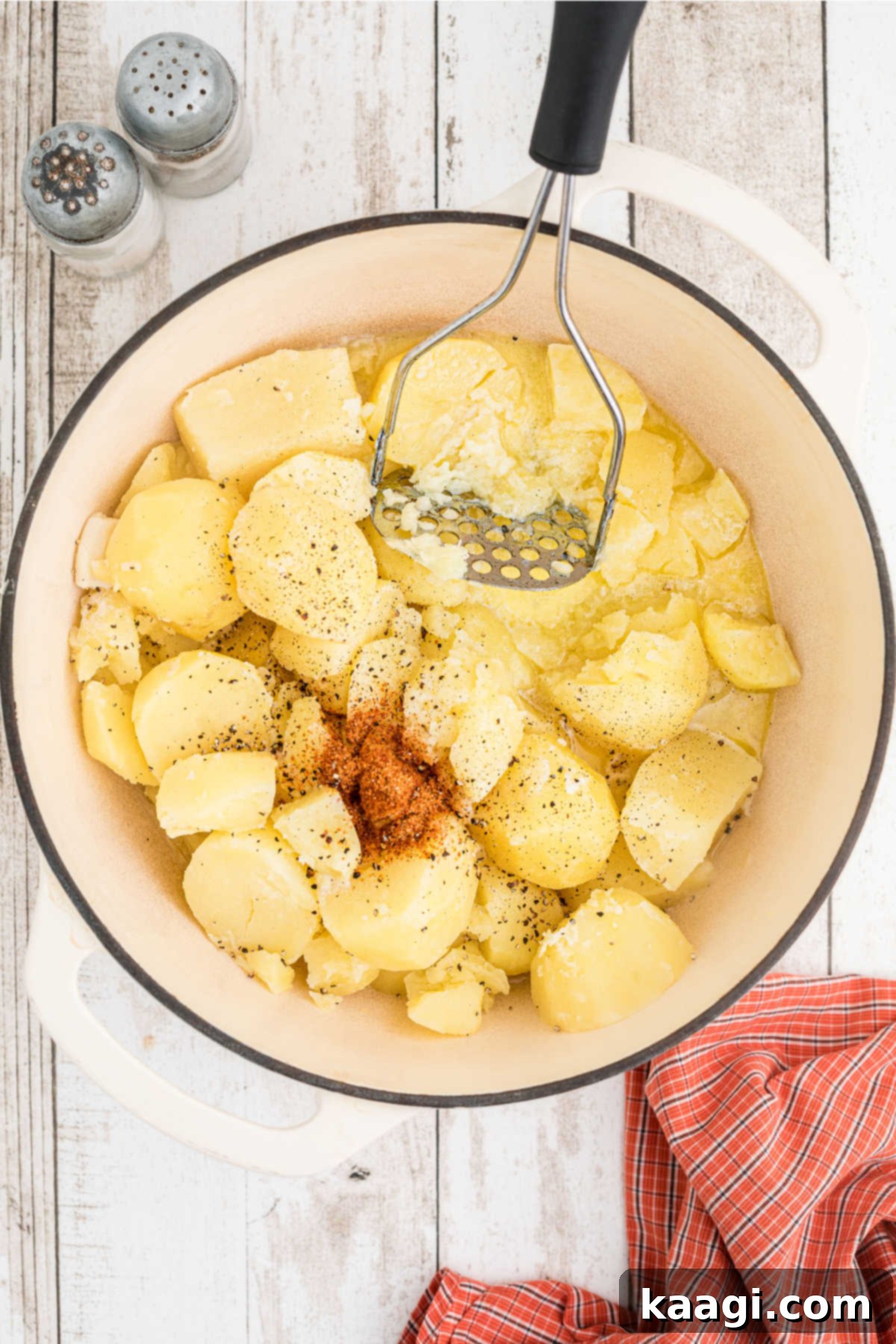 Tender potatoes in a large pot, with seasonings, warm milk, and melted butter added, ready to be mashed.