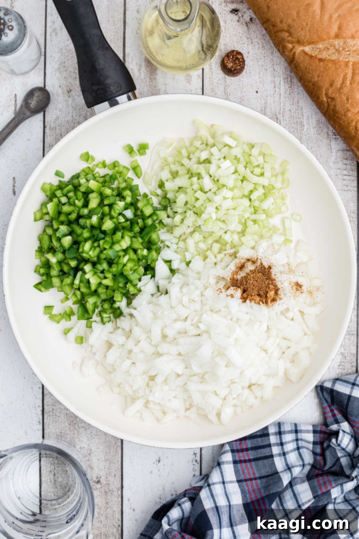 Chopped onions, green bell peppers, and celery in a large skillet, ready to be sautéed.