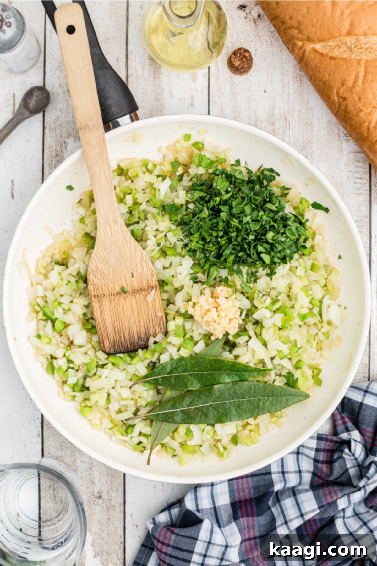 Bay leaves and minced garlic being added to the sautéed vegetables in a skillet.