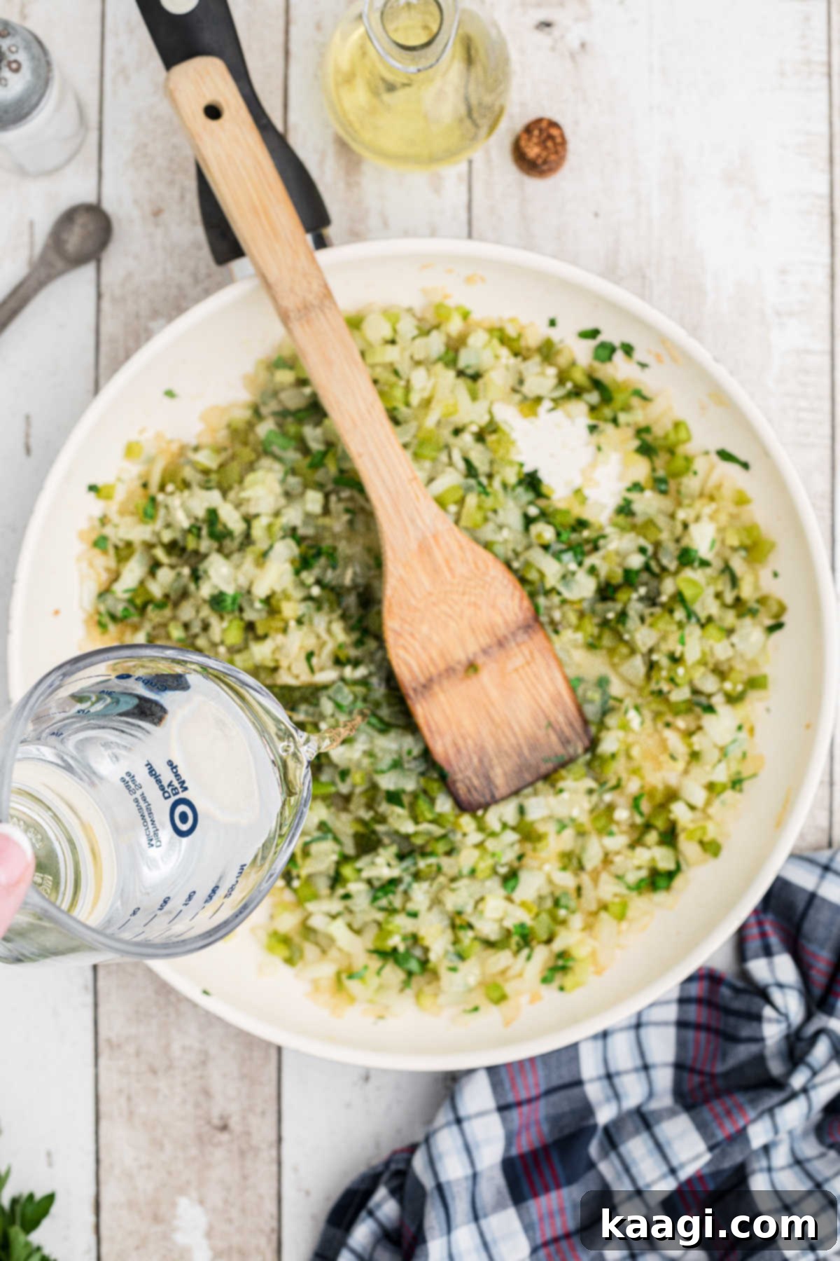A stream of water being poured into the skillet containing cooked vegetables and aromatics.