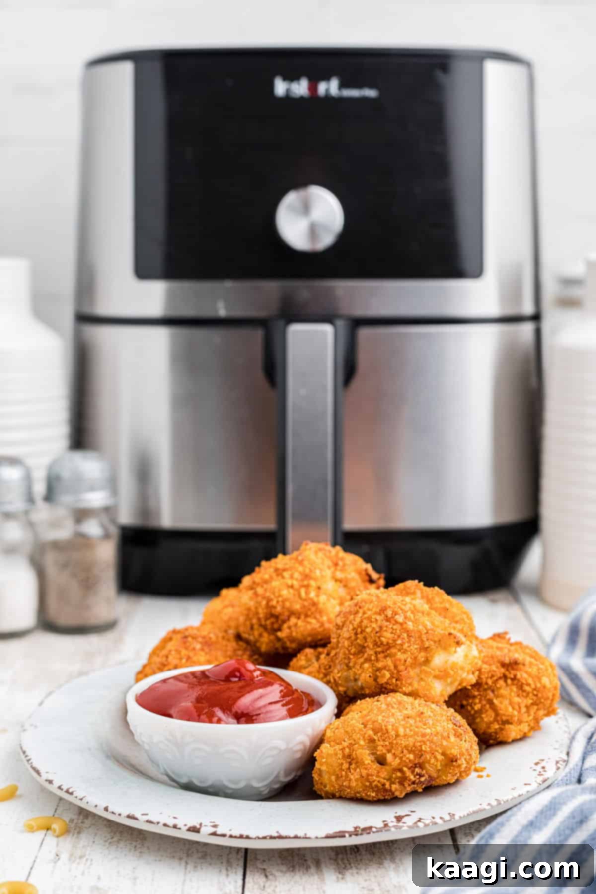 Crispy Air Fryer Mac & Cheese Poppers 2 A plate full of crispy Air Fryer Mac and Cheese Bites, golden-brown and ready to eat, with an air fryer visible in the soft background.