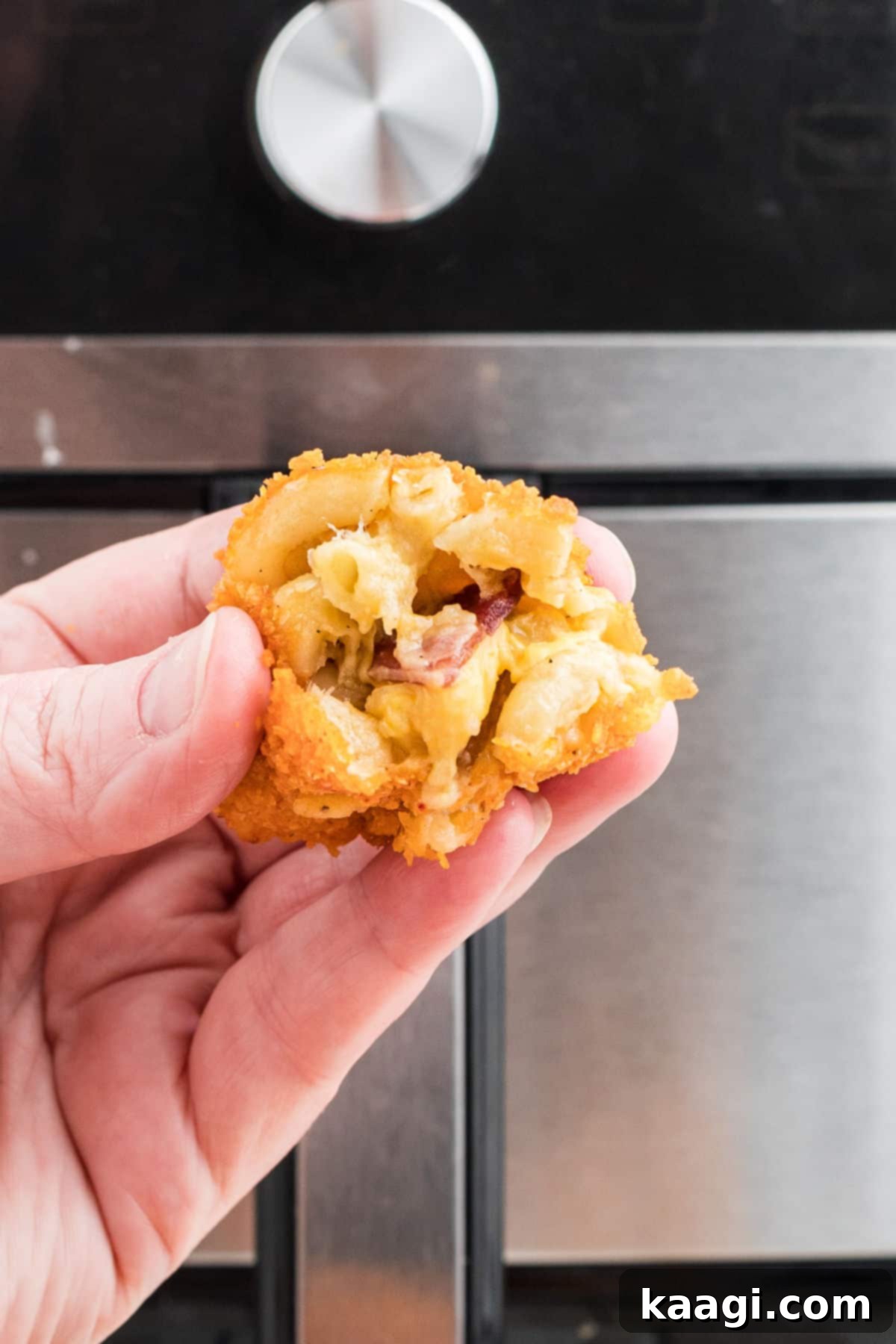 Crispy Air Fryer Mac & Cheese Poppers 10 A hand gently holding a single golden-brown Air Fryer Mac and Cheese Bite, showcasing its crispy exterior, with an air fryer in the blurred background.