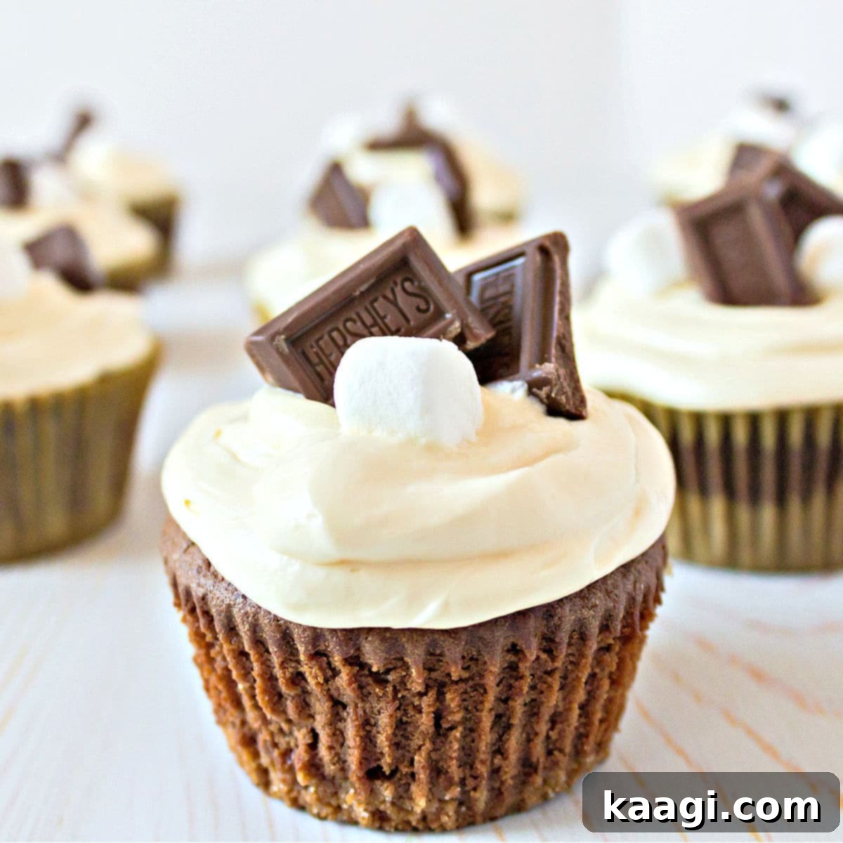 S'mores cupcakes lined up in a row with a toasted marshmallow and piece of chocolate on top of each, highlighting their decadent appearance.