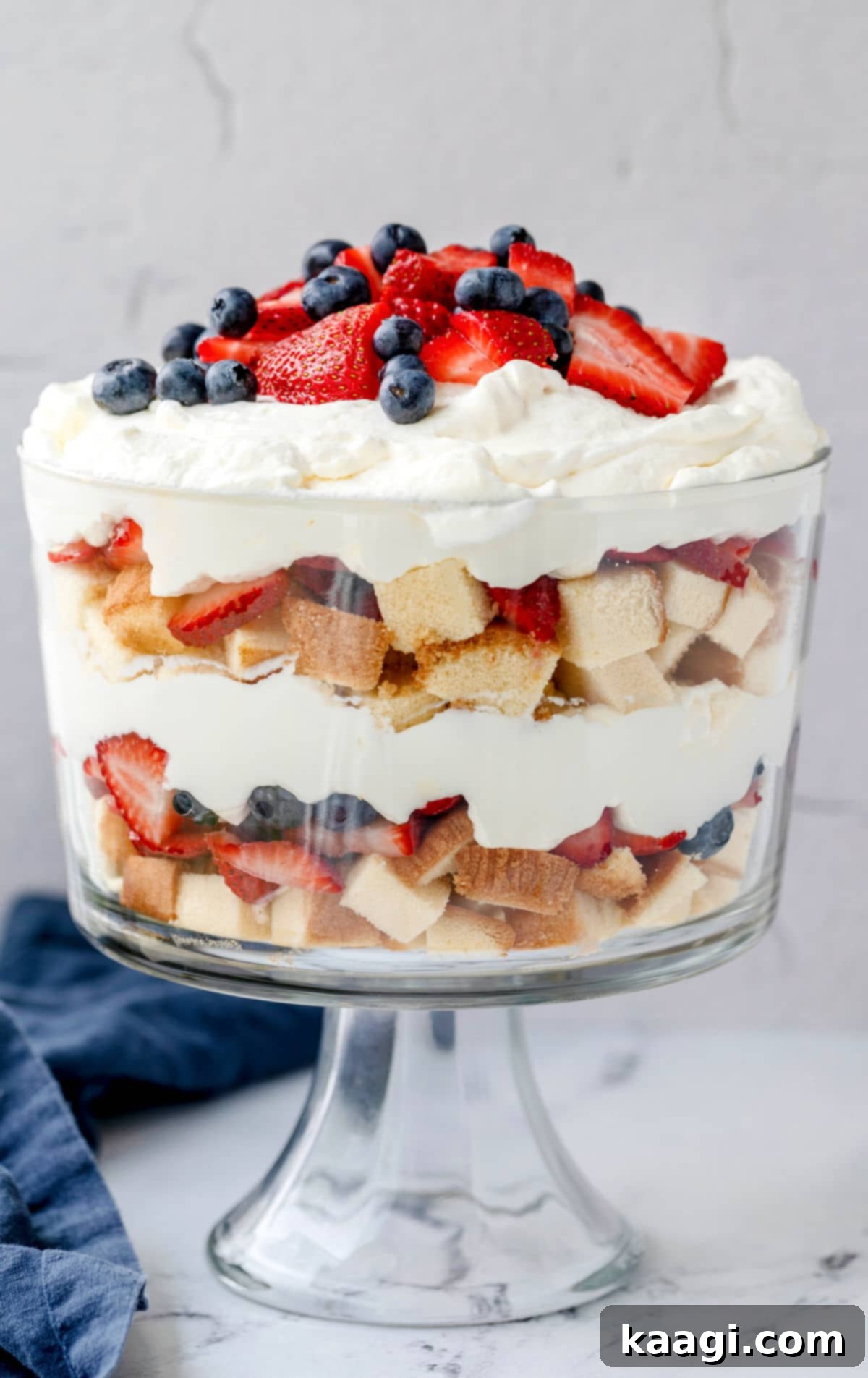A beautiful Red White and Blue Trifle, showing layers of cake, pudding, whipped cream, strawberries, and blueberries.