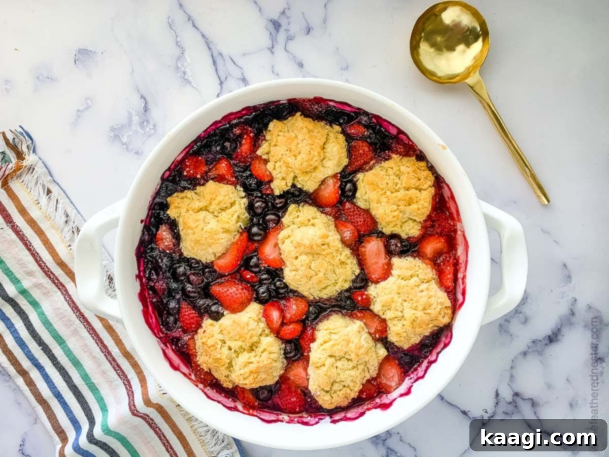 A warm Strawberry Blueberry Cobbler, showcasing a golden biscuit topping over a vibrant fruit filling.