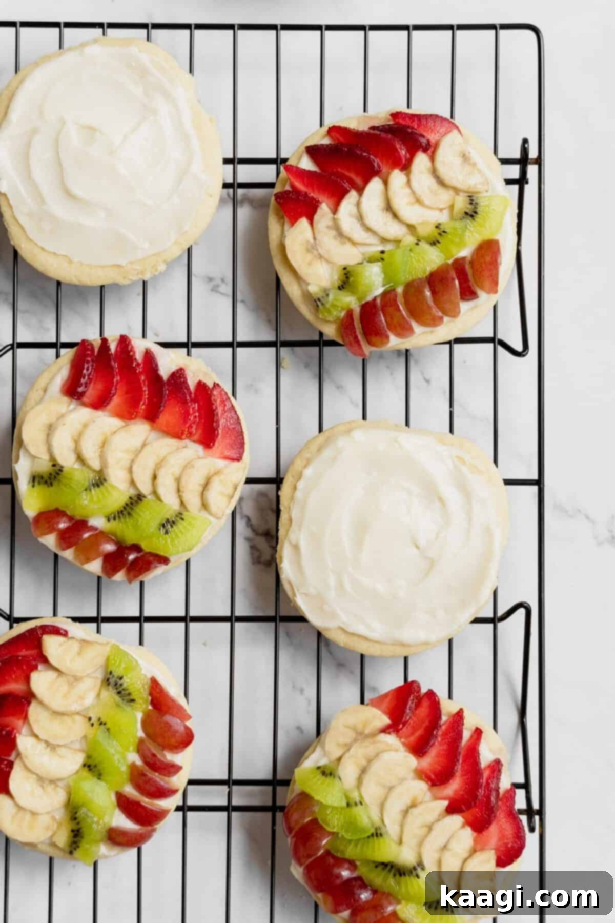 Mini fruit pizza cookies with cream cheese frosting, topped with an assortment of fresh berries and kiwi slices.