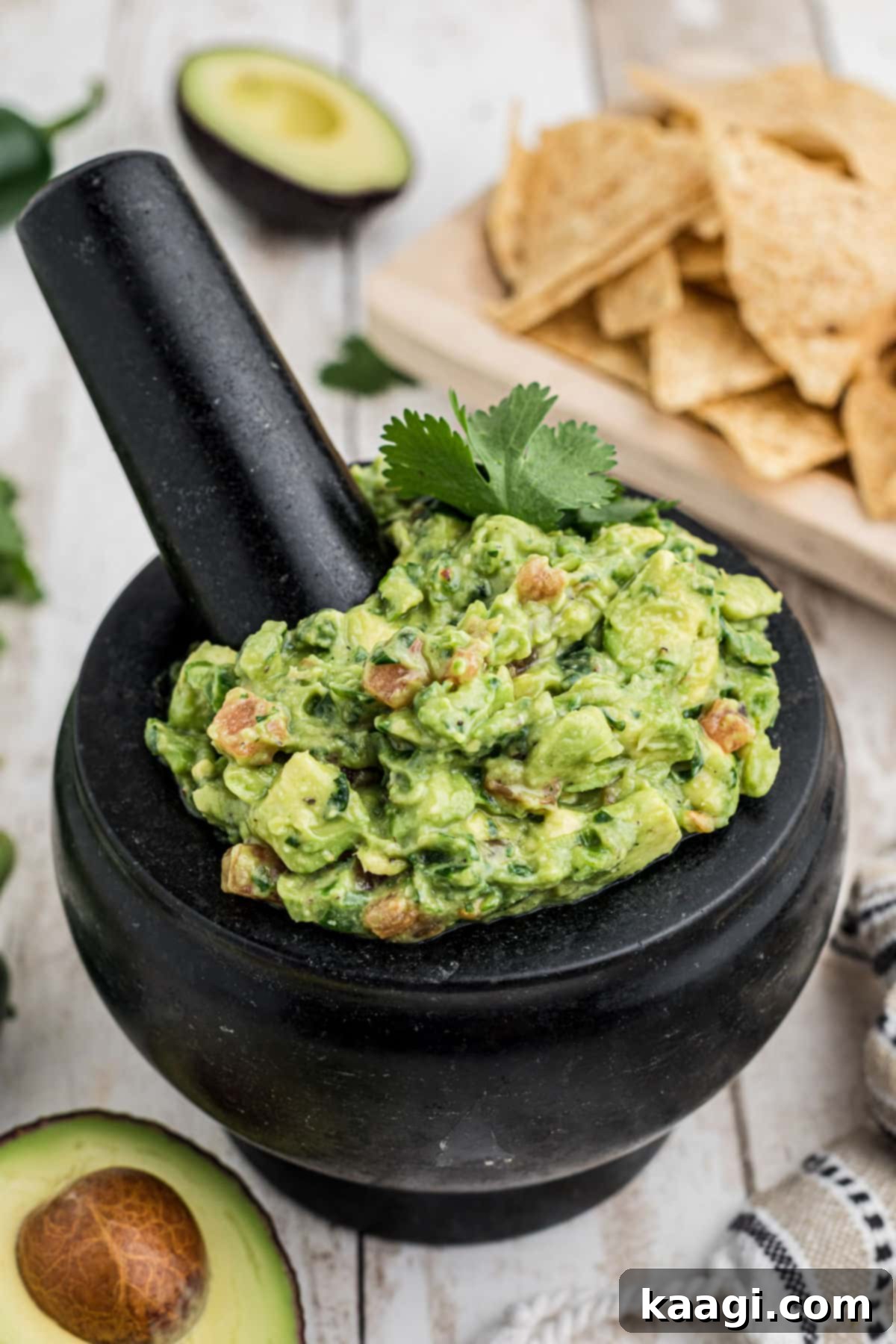 A mortar and pestle filled with creamy, chunky green guacamole, garnished with fresh cilantro and a lime wedge.