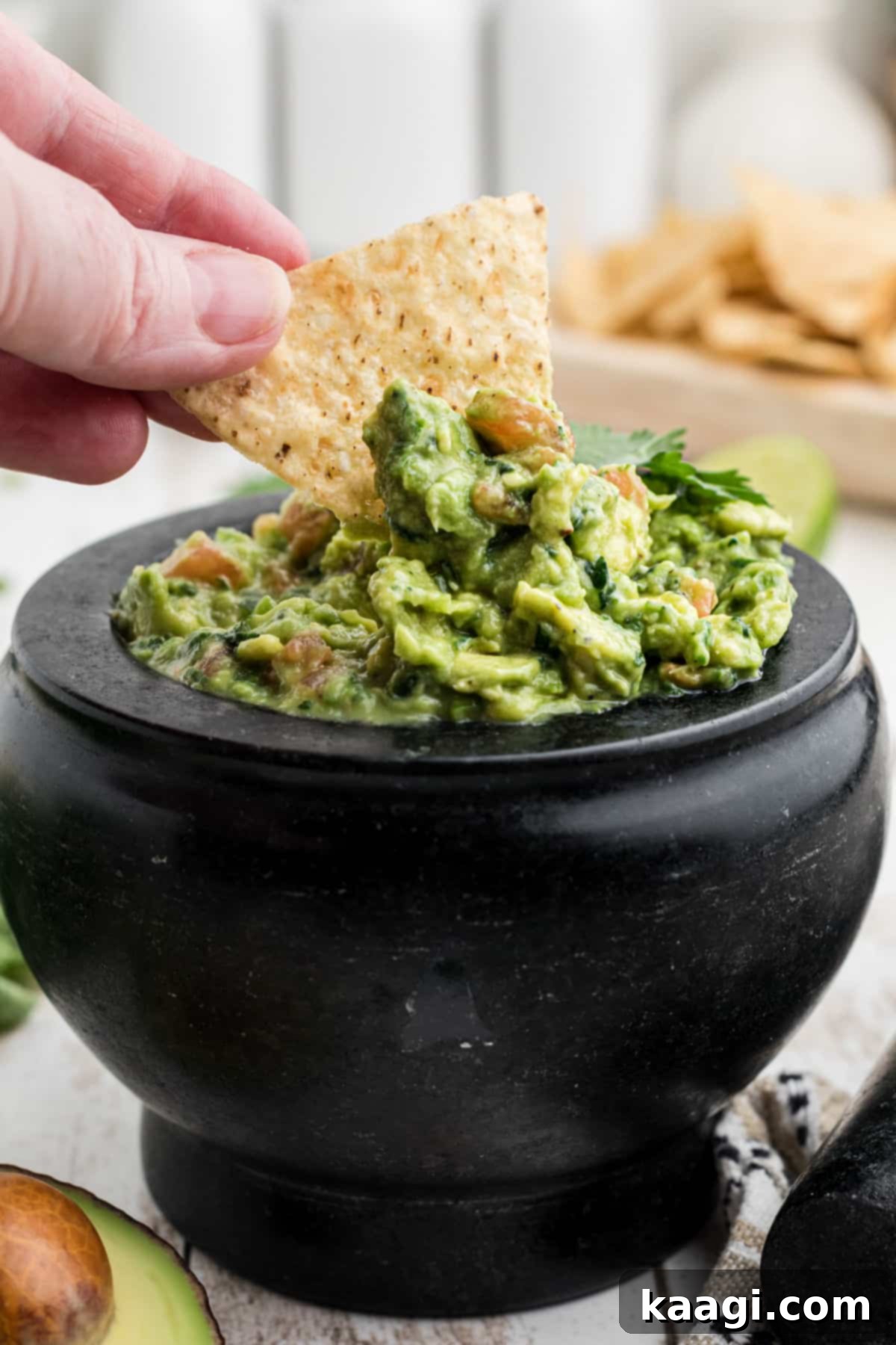 A hand dipping a crispy tortilla chip into a molcajete full of fresh, green guacamole.