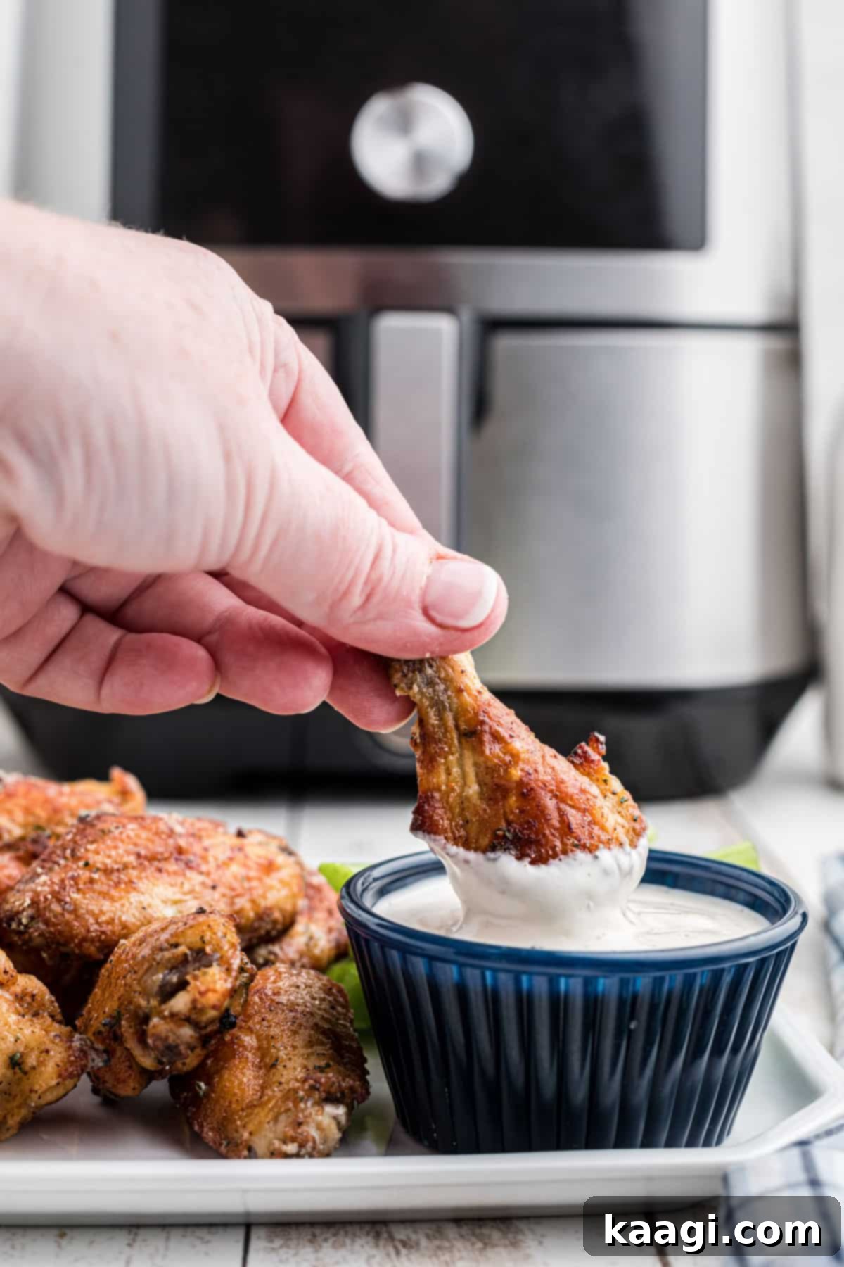 Crispy Air Fryer Ranch Wings 5 A hand dipping an air fried ranch chicken wing into some creamy ranch dip, highlighting the crispy texture.