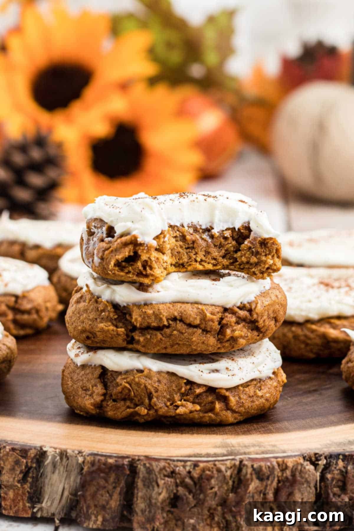 A stack of three pumpkin spice cookies with a bite taken from one, topped with creamy frosting.