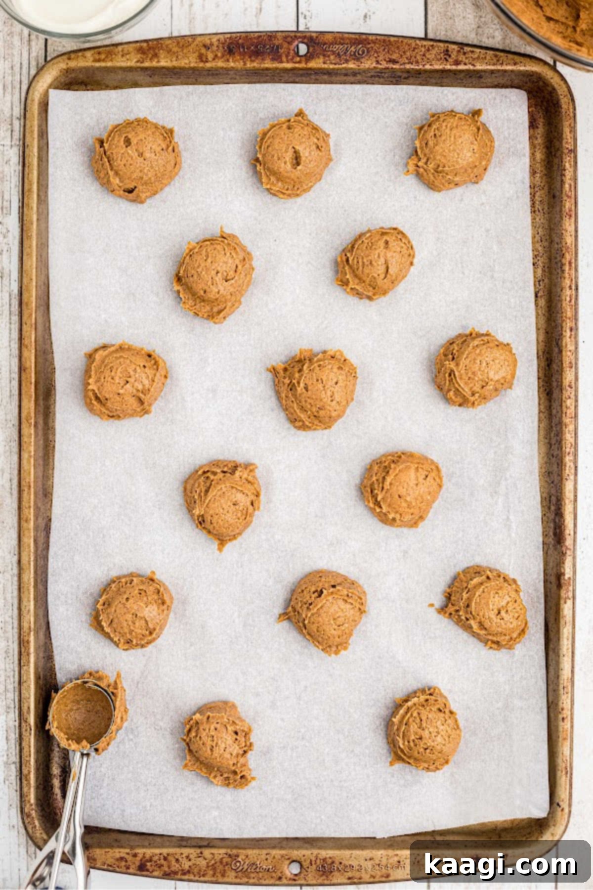 Scoops of pumpkin spice cookie dough being carefully placed onto a baking sheet lined with parchment paper.