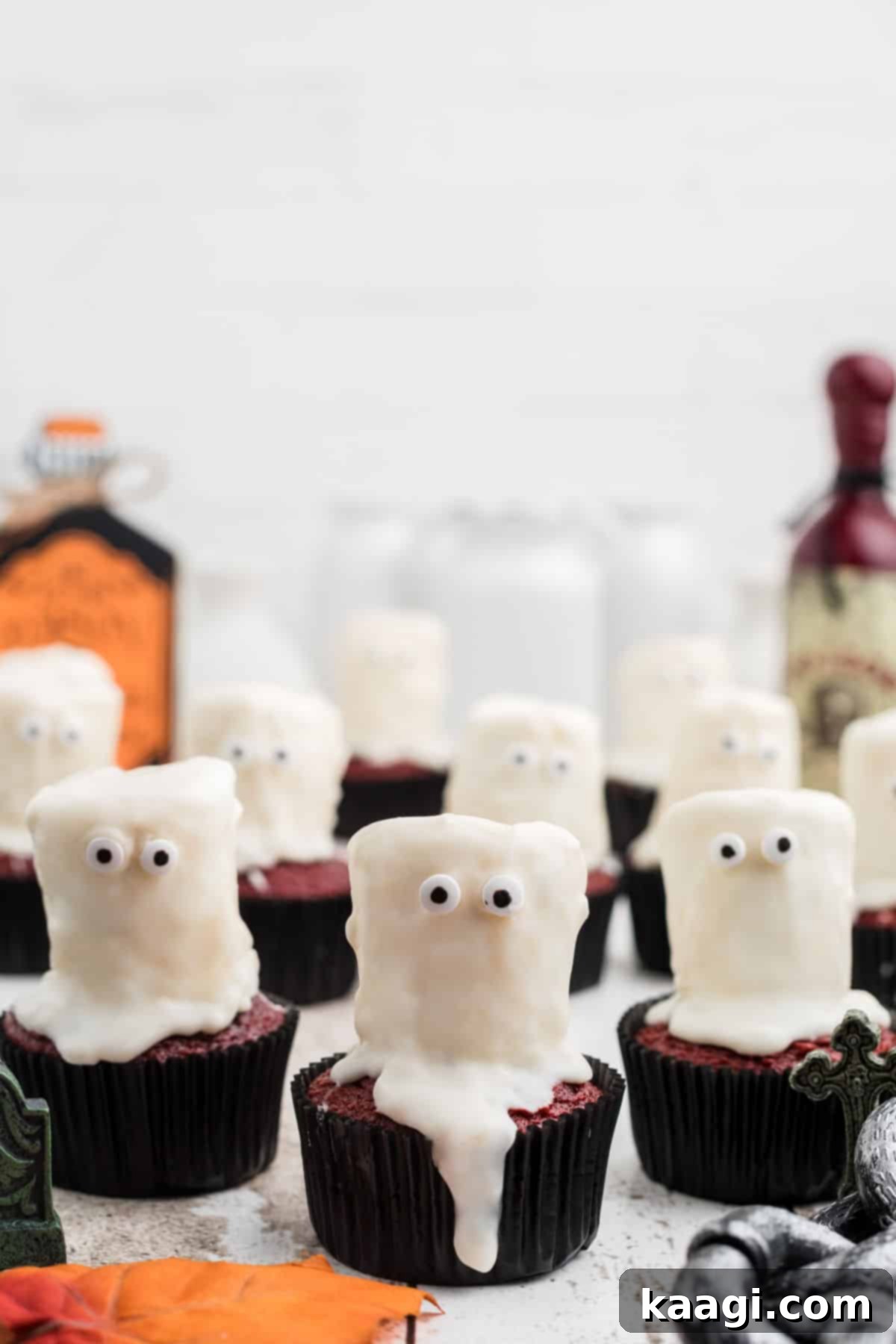 Fluffy Phantom Cupcakes 2 A row of ghost cupcakes decorated for Halloween, featuring white marshmallow ghosts with candy eyes on top of dark cupcakes.