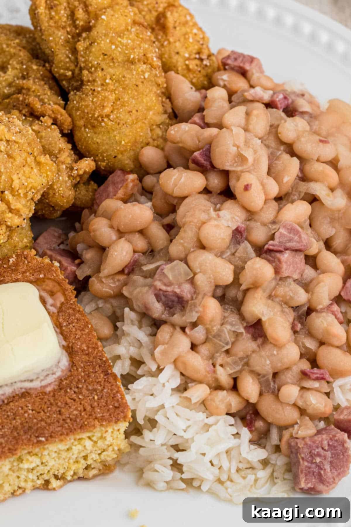 close up image of white beans on top of rice with catfish and cornbread peeking in