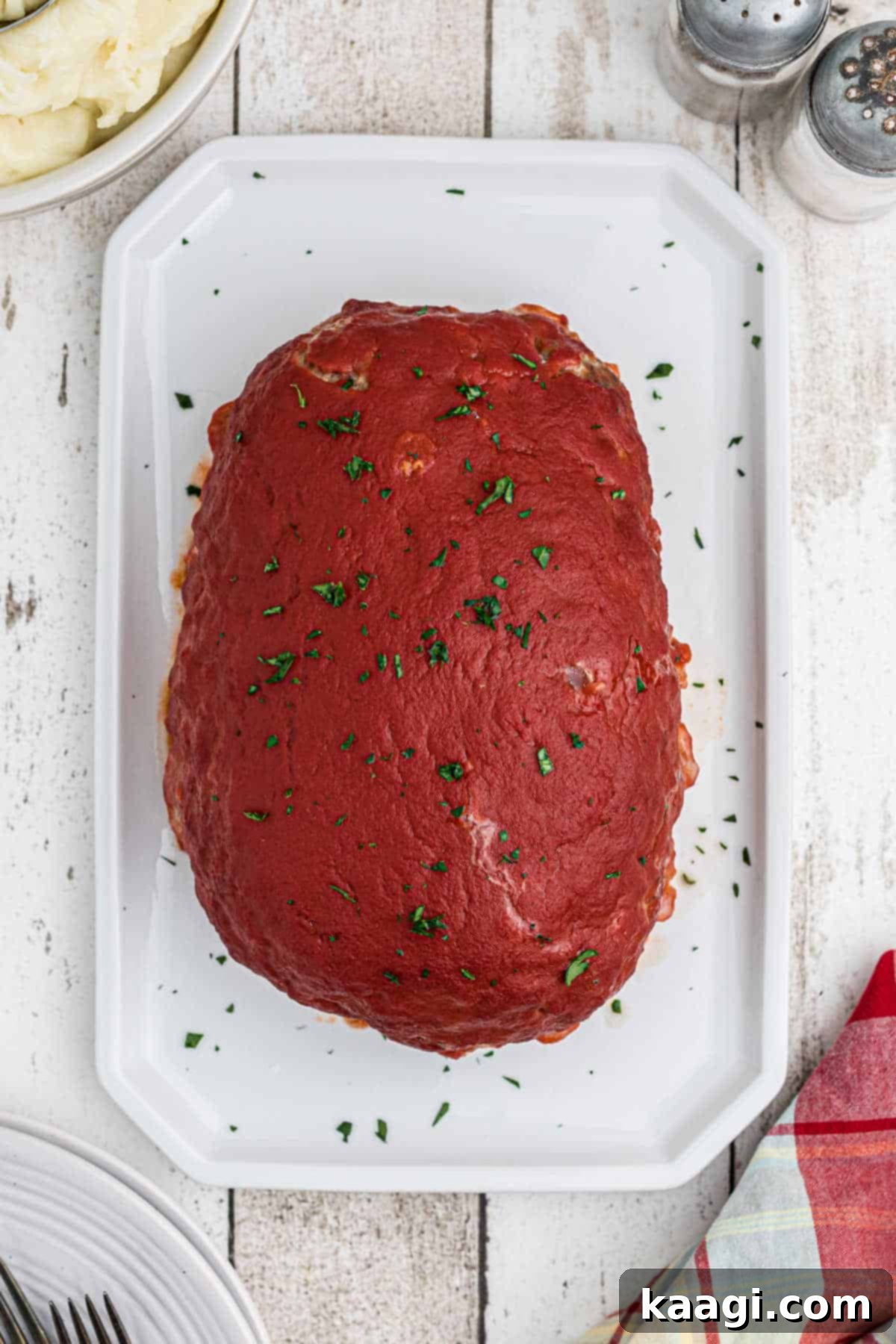 An appetizing overhead shot of a freshly baked venison meatloaf, generously topped with a rich, glossy tomato sauce glaze, glistening under the light and ready for serving.
