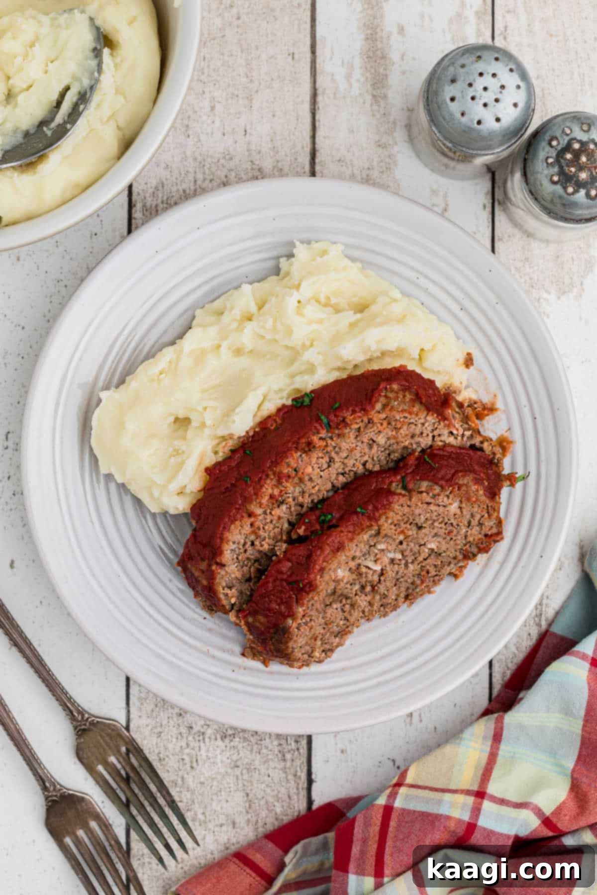 An overhead shot of a perfectly plated dish featuring a generous slice of venison meatloaf accompanied by creamy mashed potatoes, all drizzled with the savory meatloaf glaze.