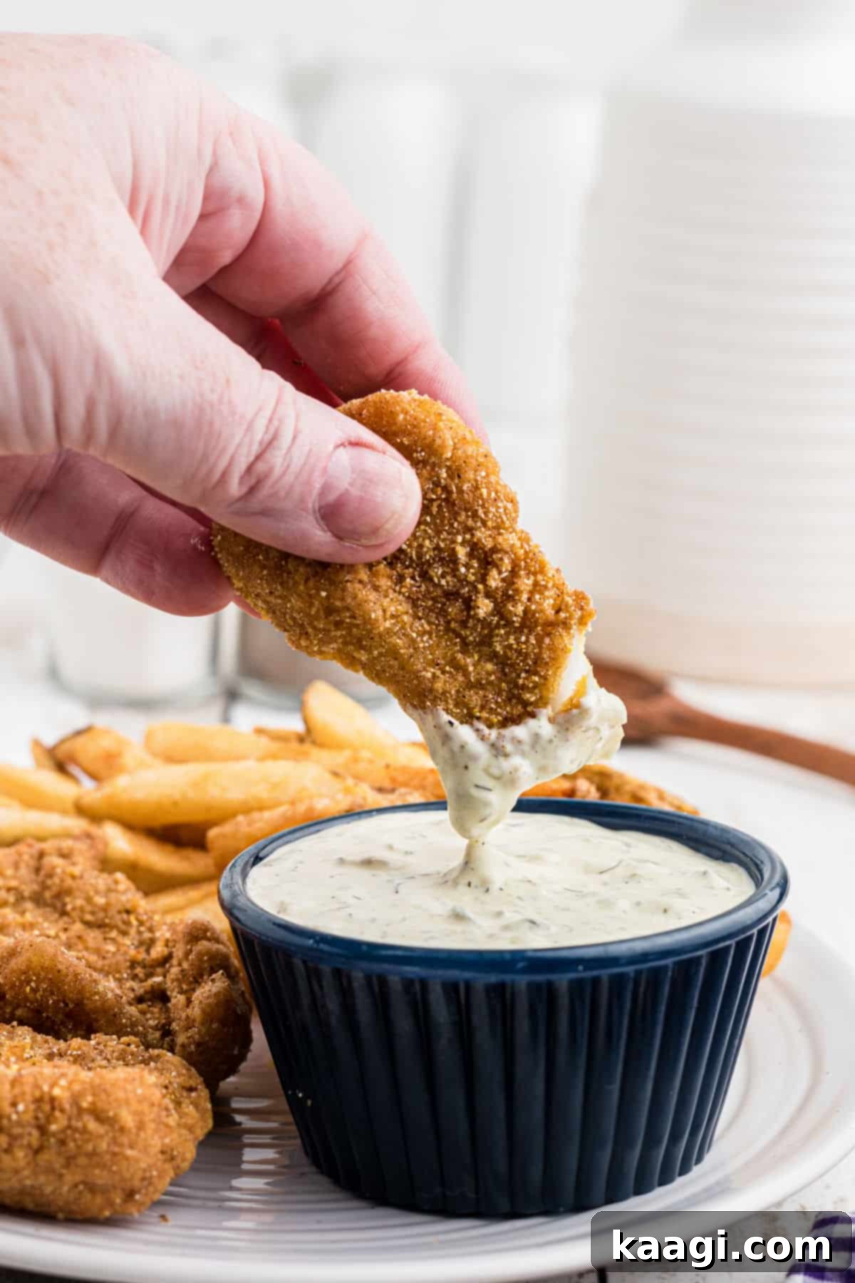 A piece of golden-fried fish being dipped into a small white bowl of creamy Southern Tartar Sauce.