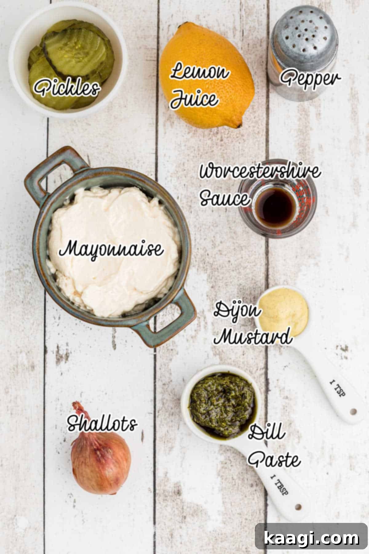 Individual ingredients for Southern Tartar Sauce, including a jar of mayonnaise, dill pickles, fresh lemon, a shallot, and spices, laid out on a wooden surface.