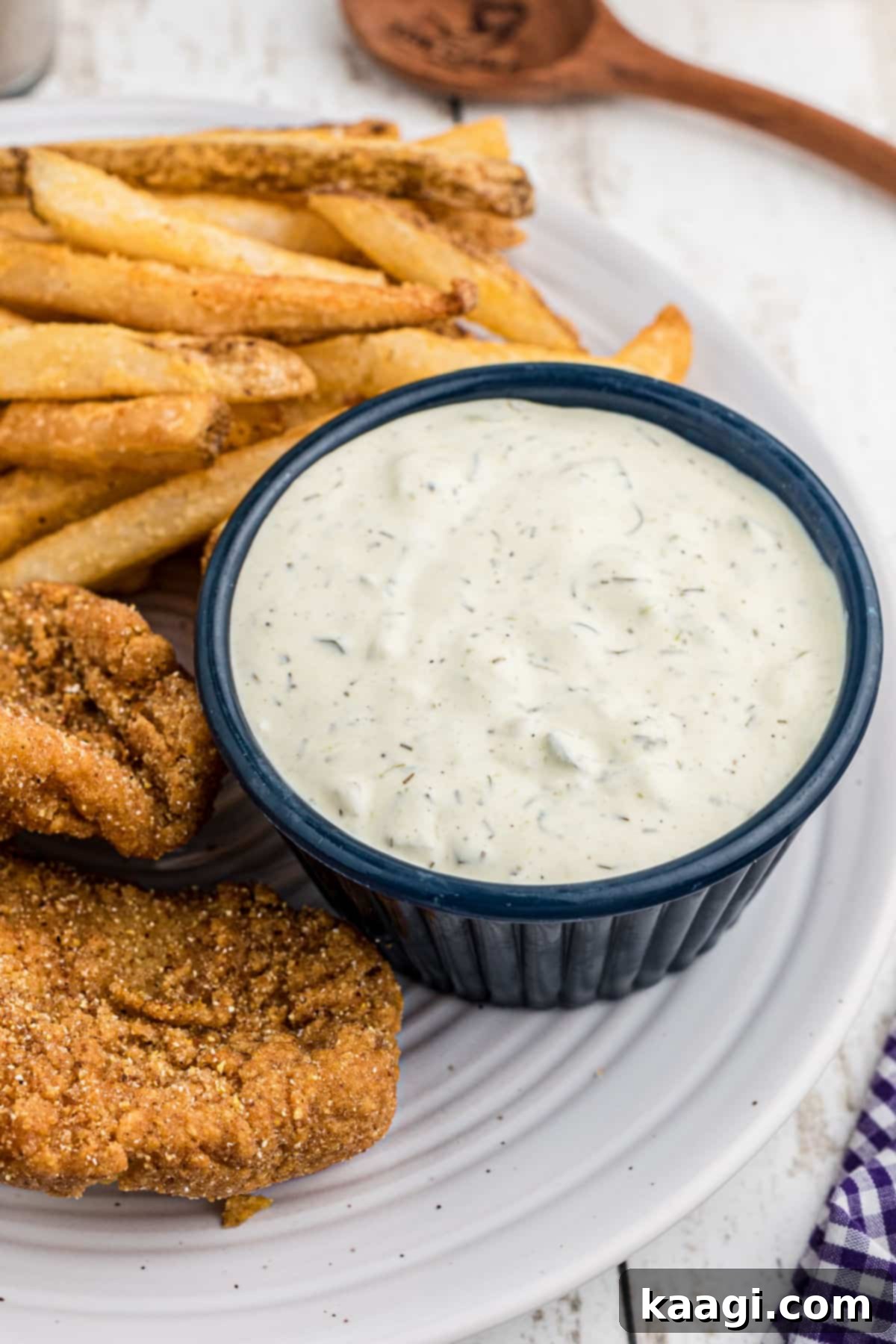 An overhead view of a bowl of creamy Cajun Tartar Sauce, with several pieces of golden-brown fried fish arranged invitingly on the side.