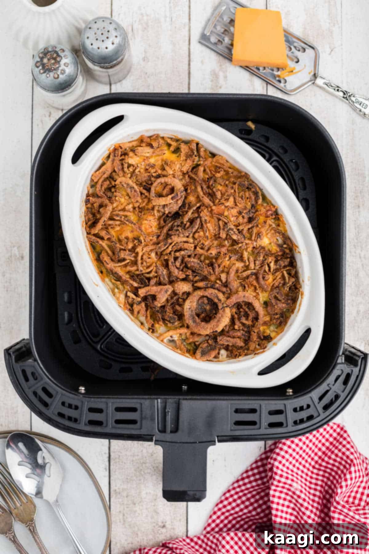 A golden brown green bean casserole in a small dish, nestled inside an air fryer basket, ready to be served.