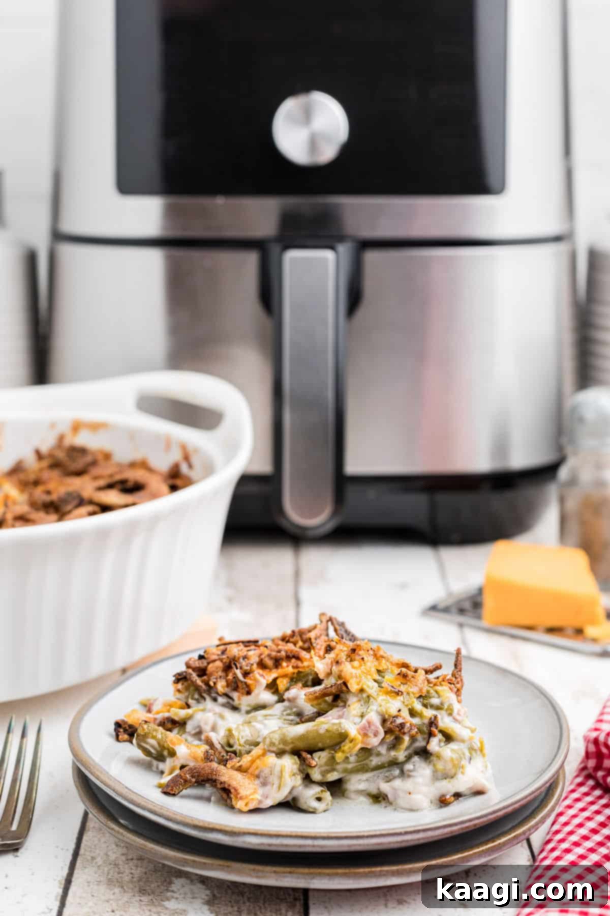 A dish with a serving of air fryer green bean casserole in the foreground, with an air fryer blurred in the background.