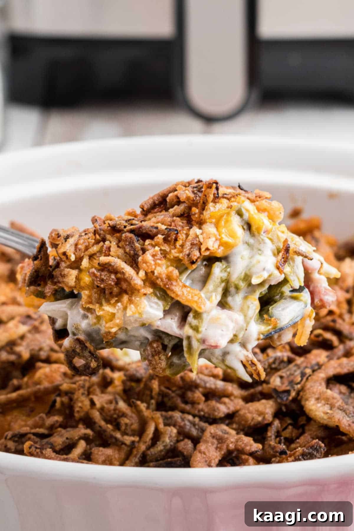 A close-up shot of a serving of air fryer green bean casserole on a white plate, showing the crispy fried onion topping and creamy interior.