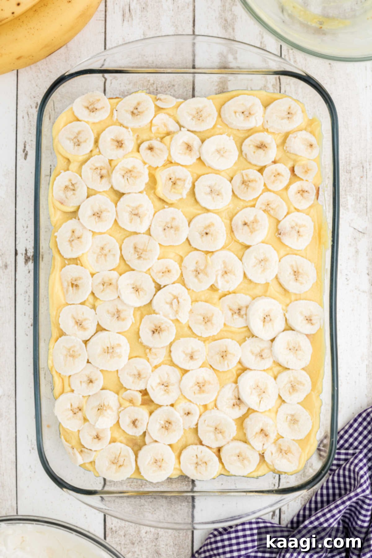 Sliced bananas and pudding being spread into a baking dish.