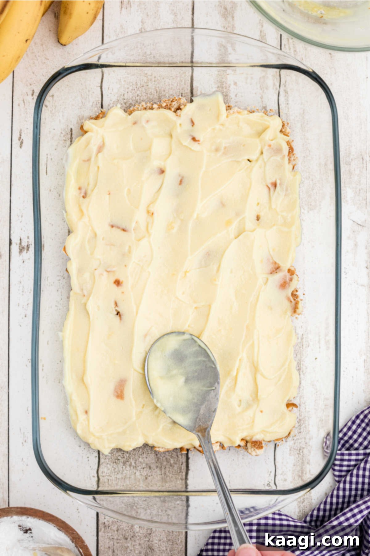 A baking dish with pudding being spread on top of crushed cookies.