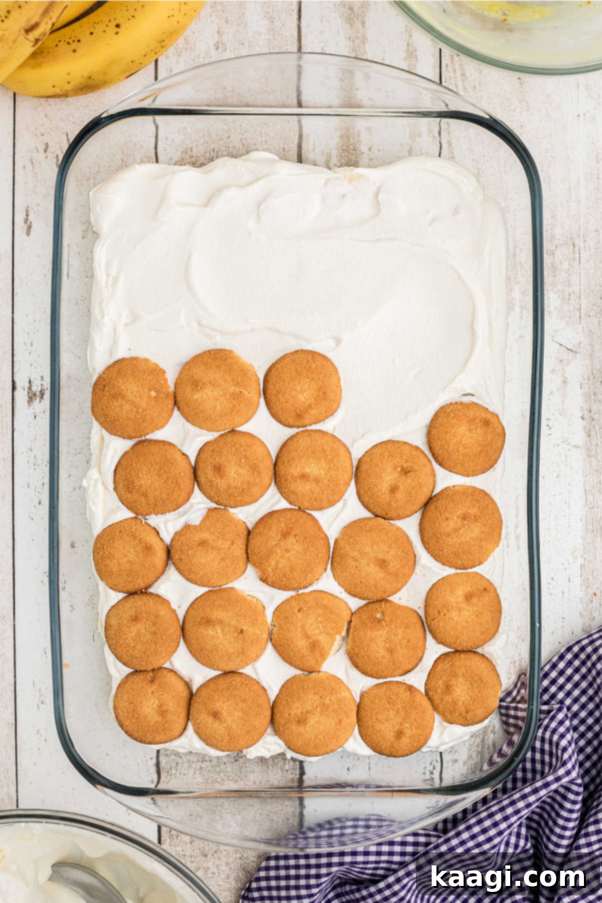 Vanilla wafers being laid out on top of a cream layer in a baking dish.