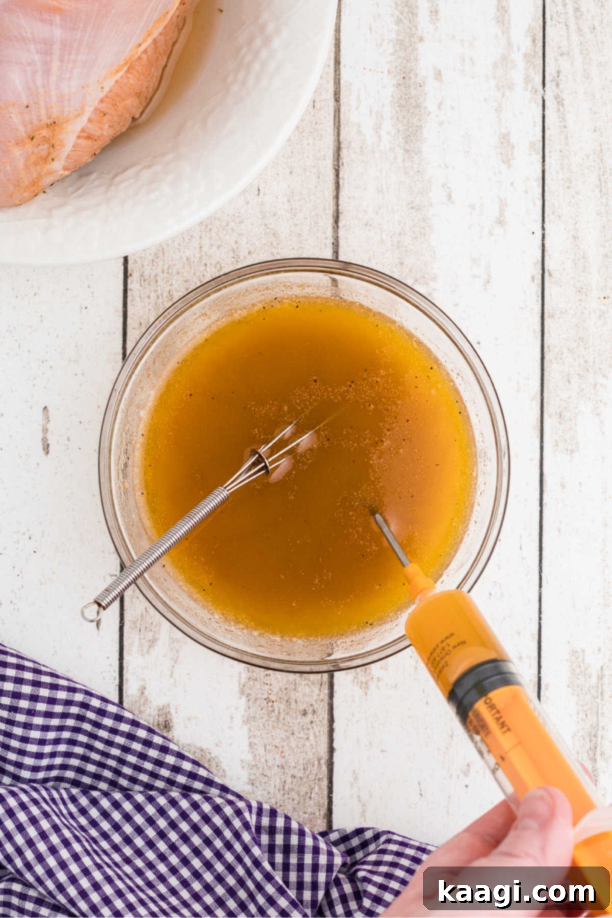 A bowl full of seasonings and marinade, with a syringe filling up.