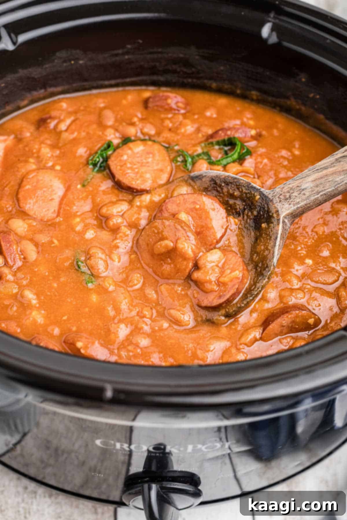 Smoky Kielbasa and Sweet Baked Beans Slow Cooker Delight 4 Close up side view of a crock pot with kielbasa and baked beans with a spoon digging in, showing the rich texture.