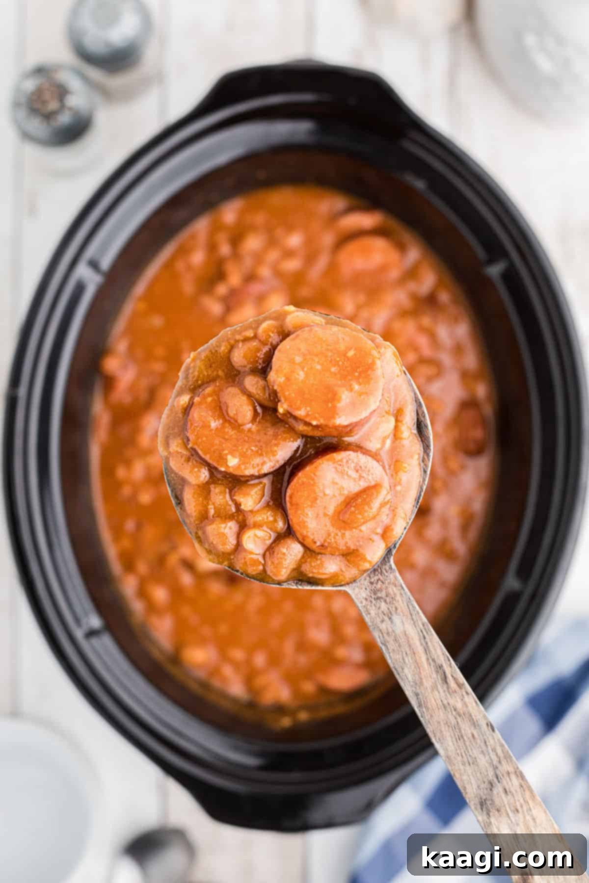 Smoky Kielbasa and Sweet Baked Beans Slow Cooker Delight 5 Overhead shot of a spoon holding some kielbasa and baked beans over a slow cooker in the background.