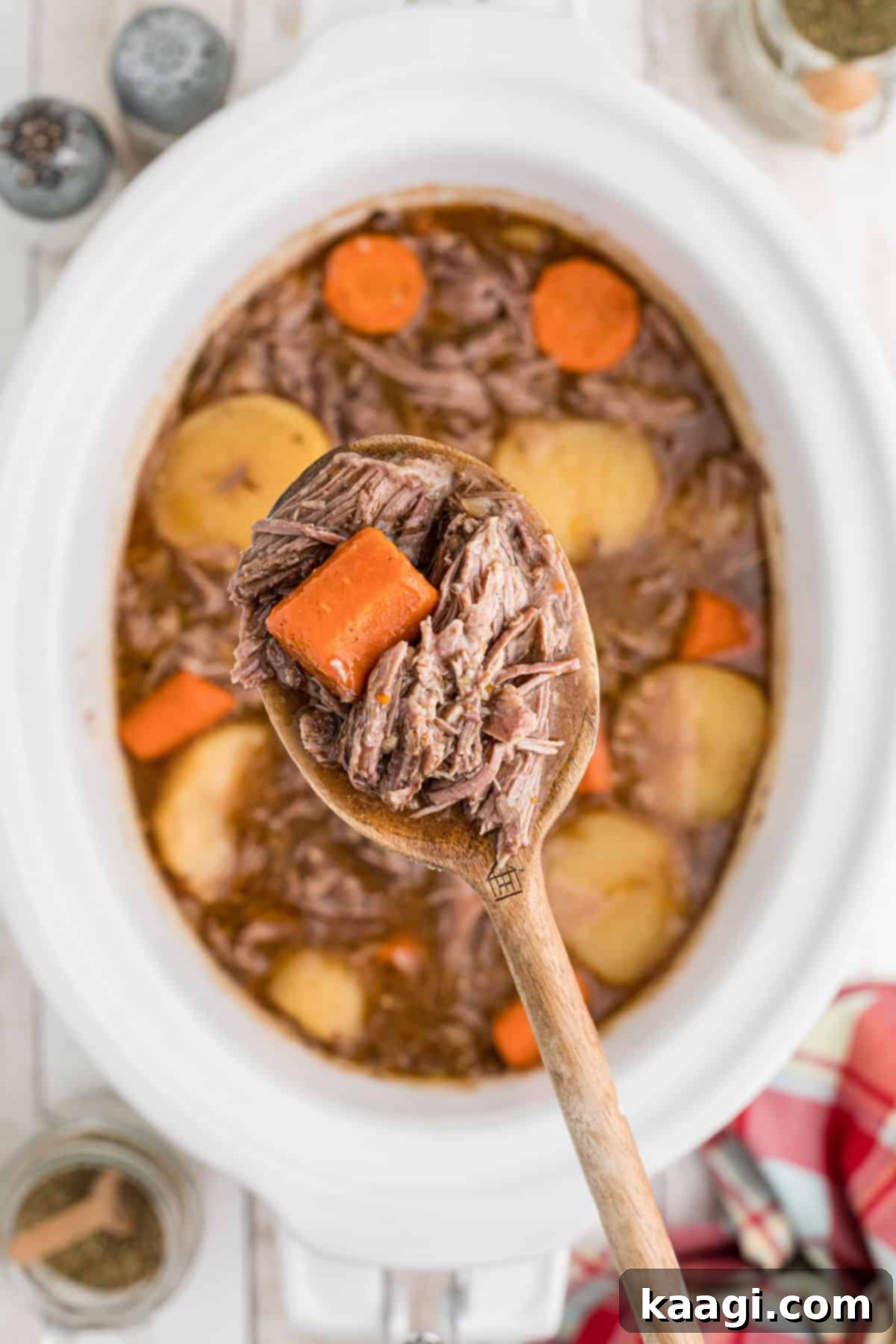 Tender Slow Cooker Tri Tip Roast 5 A spoon full of tender tri tip roast hovering above a slow cooker filled with gravy, carrots, and potatoes, ready to be served.