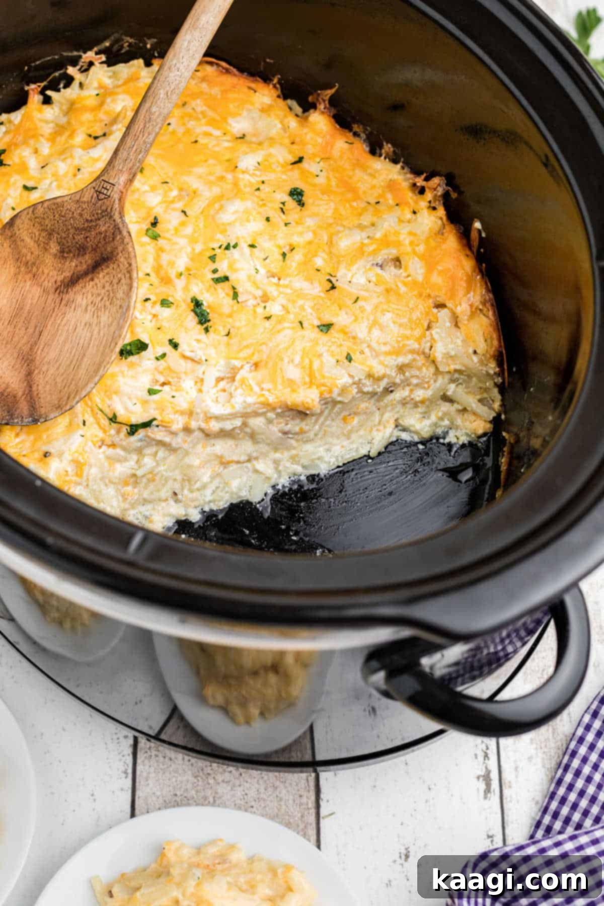 another image showing cheesy crock pot hash brown casserole with a bunch gone and a spoon resting on top.