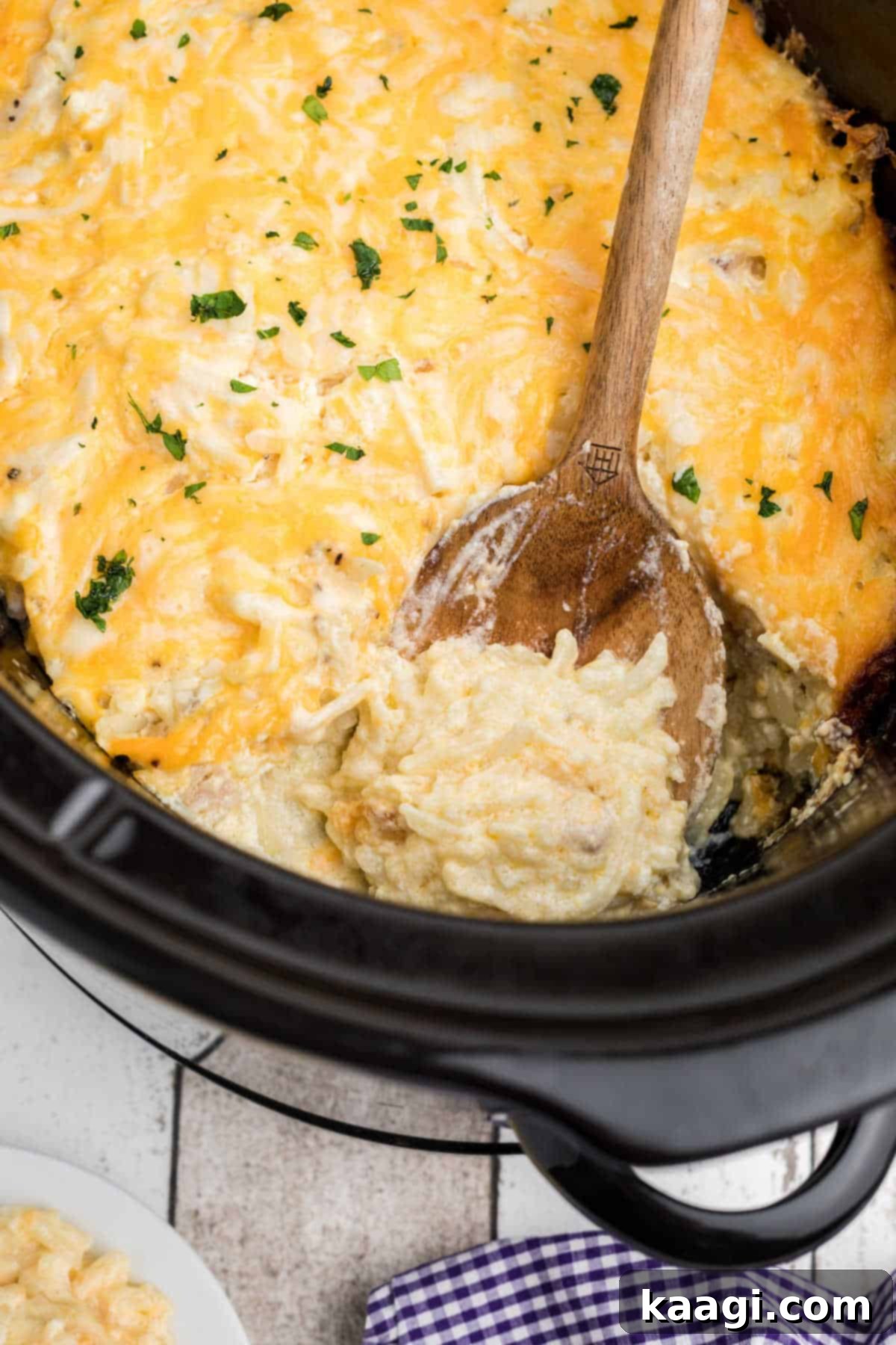 A crockpot full of cracker barrel hash brown casserole with a spoon digging in.
